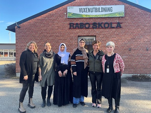 Sex kvinnor står framför en tegelbyggnad. Byggnaden har två skyltar. På dena står det Vuxenutbildning och på den andra Rabo skola.